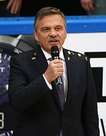 Middle-aged man wearing a dark-coloured suit speaking into a microphone
