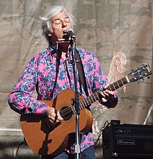 Hitchcock singing into a microphone and playing guitar