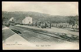 Carte postale noir et blanc. Une locomotive s'avance dans une gare de deux voies. Passagers sur le quai.