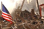 Petugas penyelamat memanjat reruntuhan dan asap di lokasi World Trade Center, dan bendera Amerika berkibar di kiri