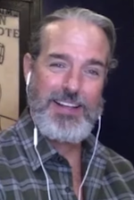 49-year-old man with slick gray and a gray beard smiling at the camera.