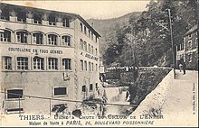 Vieille photographie de l'usine prise avec une toile pendue à une fenêtre du 1er étage où un premier diable rouge est peint au début du XXe siècle.