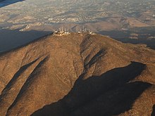 A brown mountain in the late afternoon with many TV and radio towers on top