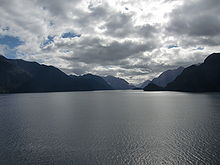 Spodní část fotografie zabírá moře, v dálce je vidět několik ostrovů a strmých břehů fjordu