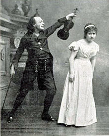 Photograph of maniac in black 19th century day clothes brandishing a violin at a frightened young woman in a full-length white frock