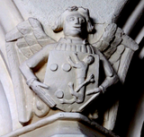 Two sculpted angels on capitals of columns of arcade, St Matthew's Church, Cheriton Fitzpaine: left: holding an escutcheon showing the arms of Courtenay (Or, three torteaux), impaling A lion (lampago?) rampant guardant coward (unknown family); right: impaling in chief A lion (lampago?) passant guardant coward, (unknown family) and in base three birds (unknown family). The arms represent a member of the Courtenay family of Upcott and one of his wives, the other with two successive wives