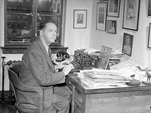Black and white photo of a middle-aged man dressed in suit, sitting a desk using a typewriter.