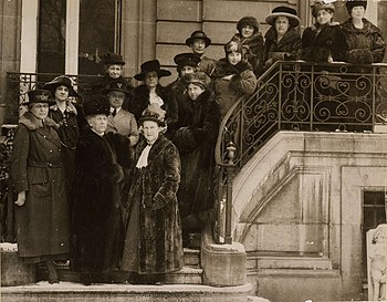 A black and white group photograph of 15 women in Edwardian dress posing on the outdoor entrance stairs