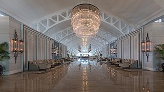Vue symétrique du spacieux hall salon avec sofas et énorme luminaire se réfléchissant au sol, à l'hôtel The Fullerton Bay, Singapour. Juin 2018.