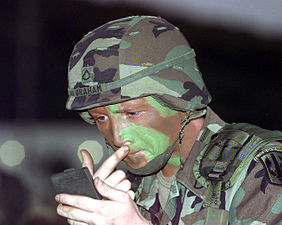 Un soldat s'appliquant un maquillage de camouflage sur le visage.