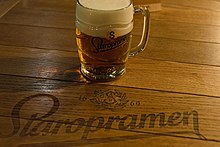 Une table en bois sur laquelle est posée une choppe de bière remplie de bière et de mousse ; la marque Staropramen est écrite à même la table.