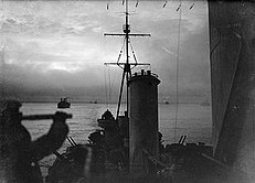 Vista do cruzador HMS Sheffield protegendo o comboio através das águas do Oceano Ártico. No fundo são os navios mercantes do comboio