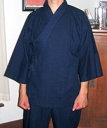 Headless photo of a man wearing an indigo wrapped-front kimono-like garment with trousers.