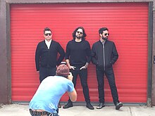 Crash Kings being photographed with a red-orange store shutter behind them