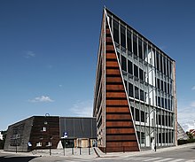 Foto eines modernen Gebäudes mit einer Fensterfront auf der einen und einer Holzverkleidung auf der anderen Seite