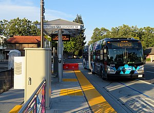 A black-and-blue bus on a city street at a bus platform