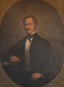 Painting of a fairly young-looking man, his right elbow leaning on a desk, turned slightly sideways to the viewer.