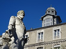 Vue en contre-plongée des étages supérieurs et du clocheton d'un bâtiment ; statue d'Henri IV au premier plan.