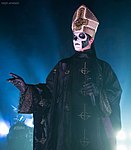 Liturgisk Papa Emeritus III Silvrig mitra med brett kantutsmyckat vitt kors försett med inverterat svartkantig ghostkrucifix i guld, samt svart mässhake med lila insida utsmyckad med ghostkrucifix i guld längs ytterkanten och yttre centerlinjen.