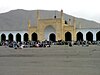 View of the Id Gah Mosque, showing the high central arch in beige with four minarets at the front and four at the back, flanked by a series of lower arches in white