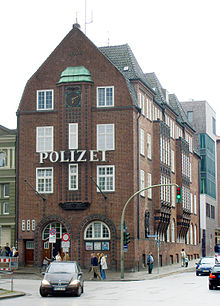 A 3 floor red-brick building, with the German word 'police' in large letters between first and second floor. The windows are white sash windows.