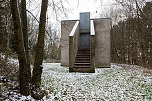 Hanspeter Demetz, Haus für August Sander, 1986/89, 550 × 550 × 550 – 250 × 550 × 110 cm, Massivbau, zementgrau verputzt. Standort: im Tal (Skulpturenpark) zwischen Hasselbach und Werkhausen