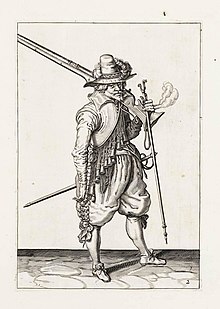 A pen and ink drawing of a soldier with a large musket over his shoulder. He wears elaborate 16th-century clothing including puffy knee breeches and a wide brimmed, tall hat with a plume.