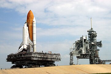 A crawler-transporter carrying Discovery (STS-114) travels the ramp to Launch Pad 39B. The vehicle's back end can be raised, keeping the Shuttle and the MLP level.