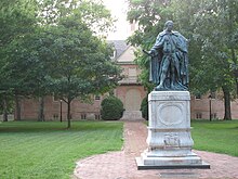 A bronze statue of a man in ermine robes on a marble plinth in front of a 17th century college building
