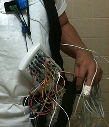 A plethora of wires are brought together in a box fastened just above the waist.