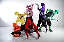 People wearing vibrant zentai suits with matching T-shirts and caps posing in a white room