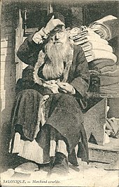 photographie noir et blanc : un homme barbu devant des rouleaux de tissu.