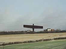 Statue viewed in the distance across fields. Railway overhead power lines can be seen in the immediate foreground