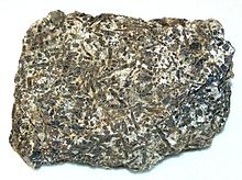 Image of a small, non-uniform and jagged white rock with black stripes of mineral running across the surface (an image of teschenite)