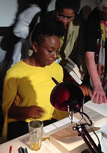 Woman sitting at a table signing books, surrounded by a crowd of other people