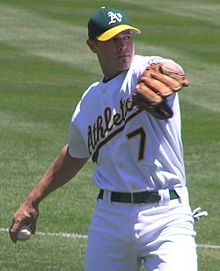 A man in a white baseball uniform and green cap