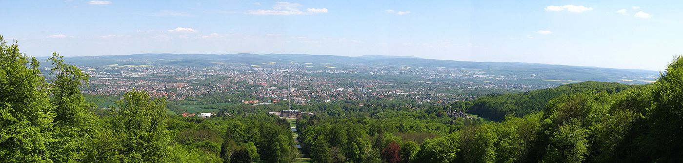 Blick vom Fuß des Herkules über den Bergpark auf Kassel: In der Bildmitte ist die zentrale Parkachse mit Schloss Wilhelmshöhe zu sehen, die ihre Verlängerung in der Wilhelmshöher Allee findet. Rechts im Bild ist auf halber Höhe die Löwenburg zu erkennen. An sehr klaren Tagen reicht die Sicht von hier sogar bis zum Brocken im Harz (In diesem Panorama allerdings nicht).