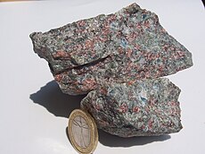 Eklogit zo západného rulového regiónu Nórska. Ako mierka slúži 1 eurová minca. Hornina na obrázku obsahuje pyroxén omfacit (zelený), granát pyrop (červený), kremeň (mliečny), kyanit (modrý) a fengit (lesklo biely).