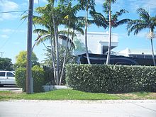 White building with a hedge and palm trees in front