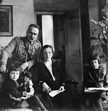 A man, a woman, and a child are on the left, posed to face the camera. To the right is a girl, drawing