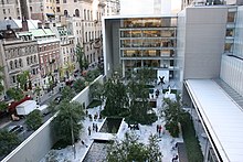 Vue de hauteur de la cour d'un bâtiment moderne, avec des arbres, des statues, des bassins (centre et droite), et de la rue adjacente (gauche).