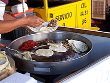 Tacos de suadero (kulay-abo) at chorizo (pula) na inihahanda sa isang takuhan