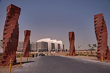 Four twisting red columns line a road leading to modern tan and white building.