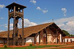 A church with a large roof and an adjacent bell tower on decorated wooden pillars