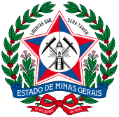 A coat of arms with a large red star in the middle bearing mining equipment. Above the star are the words "Libertas Quae Sera Tamen." The coat of arms is surrounded by a wreath of red berries and green leaves, with two stems of leaves sprouting from the bottom and framing a banner stating "Estado de Minas Gerais." A green ribbon is at the bottom; on the left tail, it says "15 de junho" and on the right, "de 1891."