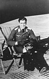 A man sitting in folding chair wearing a military uniform, a peaked cap is resting on his knees.