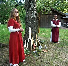 زن و مردی بیرون از خانه کنار درختی ایستاده‌اند و لباس‌های قرمز و سفید به تن دارند