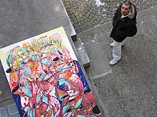 Ralf Abati steht in einem Innenhof in Zürich vor einem farbenfrohen Gemälde und wird vom 1. Stock aus fotografiert.