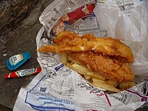 Fish ’n’ Chips mit Papierschutz vor der Druckerschwärze der Zeitung und Soßenbeutel
