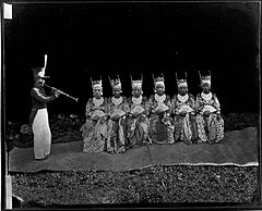 Czarno-białe zdjęcie przedstawia muzyka i grupę tancerek w tradycyjnym stroju Ternate.